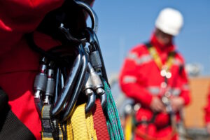 Various safety equipment with a person wearing safety equipment and a harness in the background.