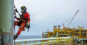 Worker in safety equipment including ropes and a harness working at heights in an industrial setting