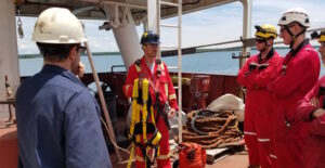 Outdoor safety training by the water with several people wearing hard hats.